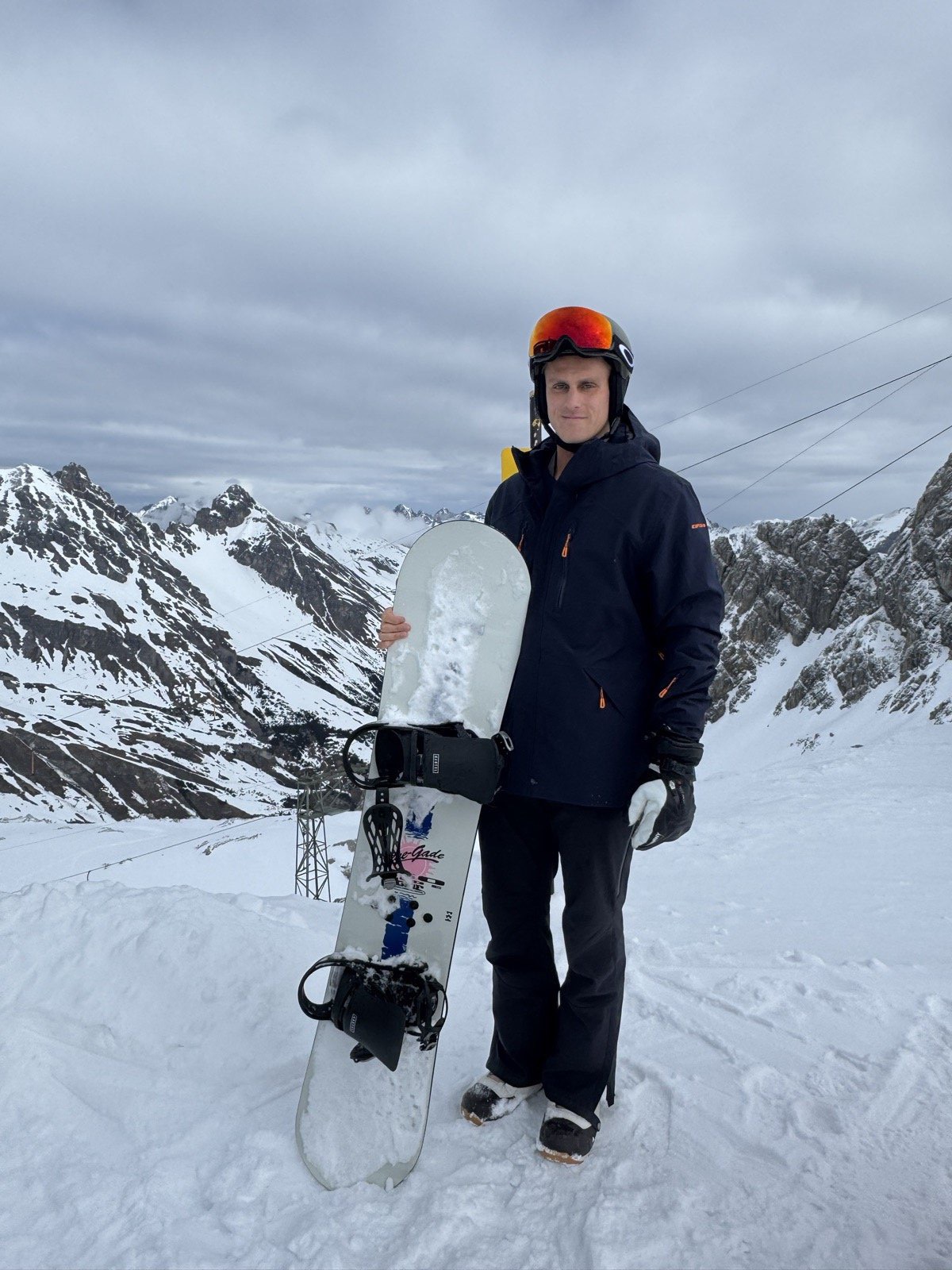 Andrew standing with his snowboard on a ridge in the Austrian Alps